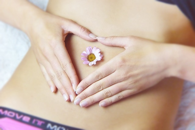 Person with a flower in the navel with their hands around in in the shape of a heart over the abdominal brain region.