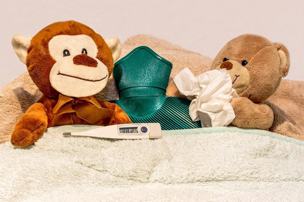 2 teddy bears with a hot water bottle, thermometer, and tissue trying to get well