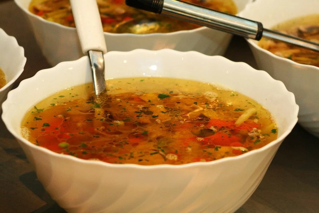 A bowl of soup with a wide variety of herbs and veggies in it.