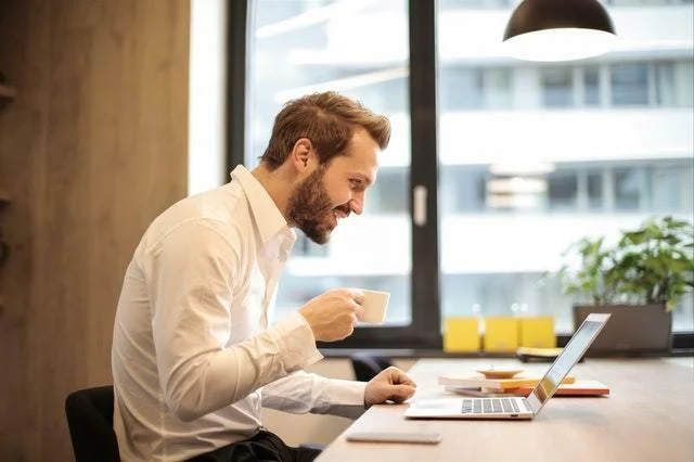 Stress, Posture, and Back Pain, Are they Linked? Person drinking coffee at a computer slouched over